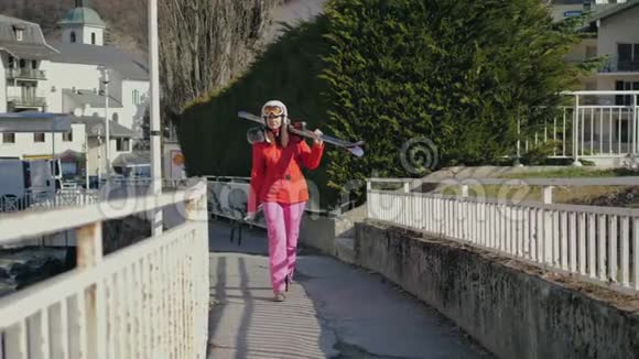 在滑雪前一位女士肩扛着她的高山滑雪板在村里行走视频的预览图