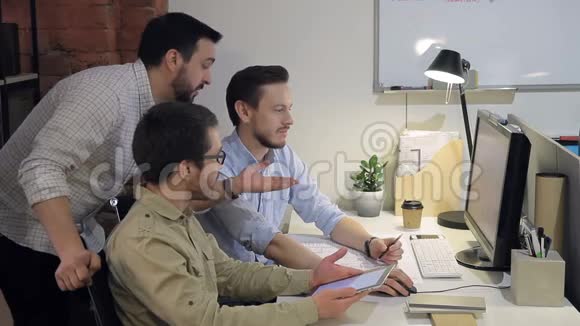 年轻的商人在办公室里看着电脑和平板电脑的屏幕比较和分析信息视频的预览图