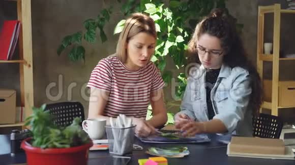 年轻的女商人设计师们坐在桌子旁谈论和选择新项目的图片他们是视频的预览图