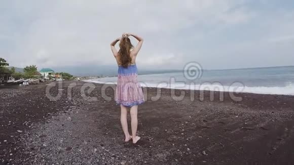 在巴厘岛一个高大的女孩沿着黑色的沙滩漫步视频的预览图