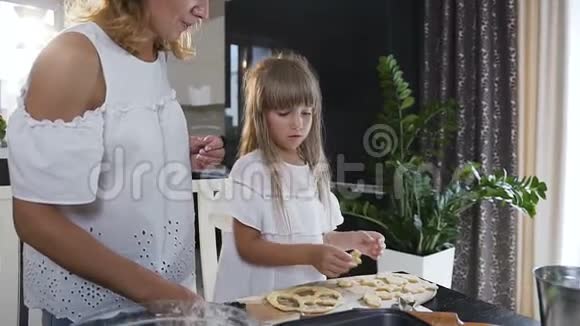 年轻的母亲和小女儿在厨房做饼干厨房里的女人和小女孩把饼干面团视频的预览图