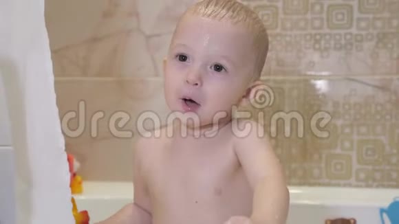 可爱的小男孩洗澡和冲洗浴缸里的小孩带着五颜六色的玩具在浴室里微笑的孩子婴儿视频的预览图