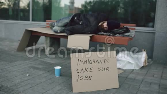 由于移民危机无家可归和失业的欧洲人带着硬纸板标志在城市大街的长椅上睡觉视频的预览图