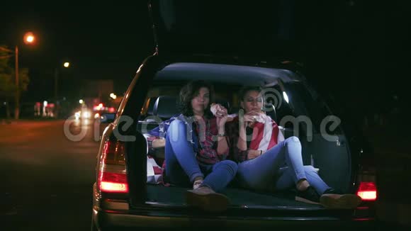 两个漂亮的女朋友坐在敞开的车厢里晚上在城里聊天吃汉堡视频的预览图