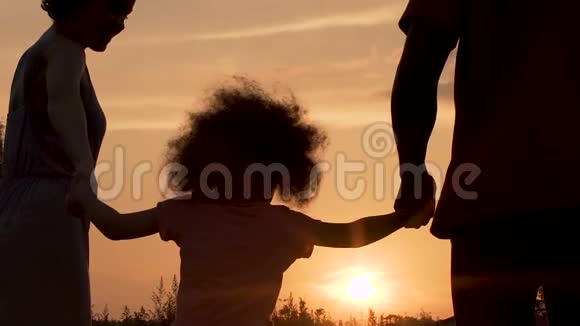 父母与小女儿在夕阳下嬉戏的剪影视频的预览图