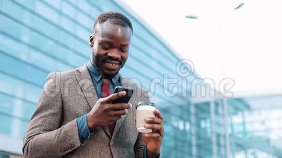 快乐的非裔美国人在他的智能手机中键入一些东西站在办公室中心附近的概念视频的预览图