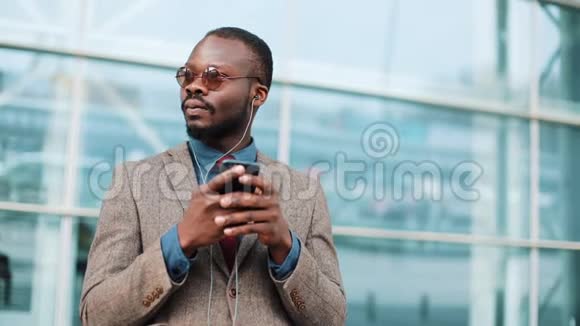 非裔美国商人的肖像使用智能手机在城市户外听耳机音乐他站着视频的预览图