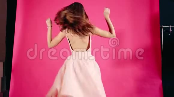 美丽的女孩穿着裙子在粉红色的背景上旋转和跳舞视频的预览图