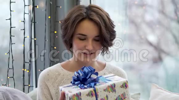 幸福的女人拿着礼物盒在窗户背景上装饰着圣诞快乐把拿礼物的女人关起来视频的预览图