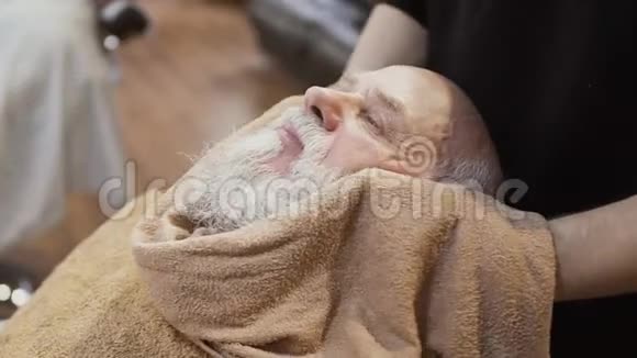 理发师在剃须前用热毛巾蒸熟成熟男人的脸视频的预览图