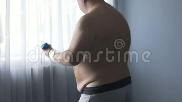 胖子积极做运动举起哑铃减肥在家锻炼视频的预览图