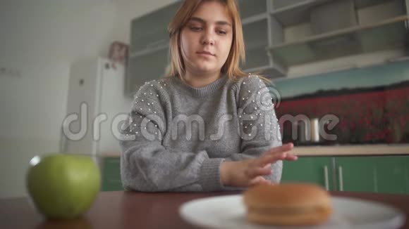 肖像丰满的女孩认为她应该吃美味的汉堡包或多汁的绿色苹果困难的选择视频的预览图