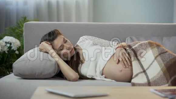 期待女人躺在沙发上轻轻地摸着肚子试图休息视频的预览图