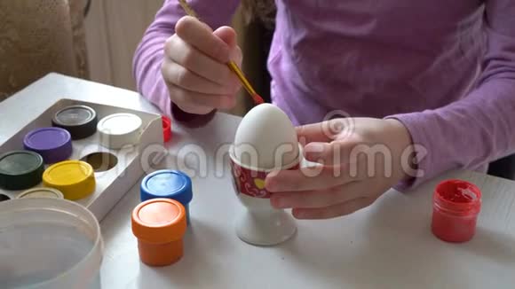 一个小女孩用画笔画画在一个白色的鸡蛋上涂上颜色坐在家里的桌子上快关门4K25fps视频的预览图