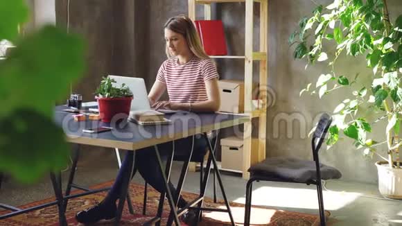年轻女子正拿着笔记本电脑坐在办公室的桌子上她的同事来了女人们开始看电视视频的预览图