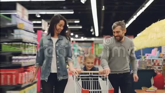 幸福的家庭父亲母亲和孩子带着购物车在超市里奔跑的慢动作微笑着视频的预览图
