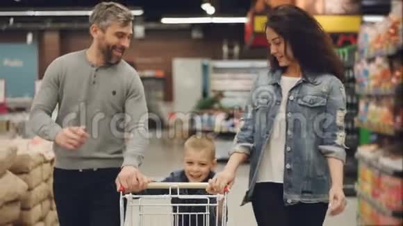 快乐的人慢动作快乐的一家人用手推车在食品店里跑来跑去男孩在推视频的预览图