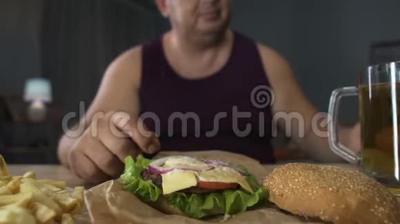 男人用沙拉叶装饰高热量汉堡准备吃肥胖视频的预览图