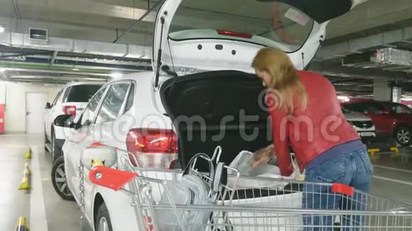 购物一个女人把袋子从手推车里放在车的后备箱里购物地下超市停车场4k视频的预览图