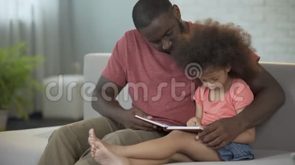 可爱的父亲看着他的小卷发女儿学习阅读视频的预览图