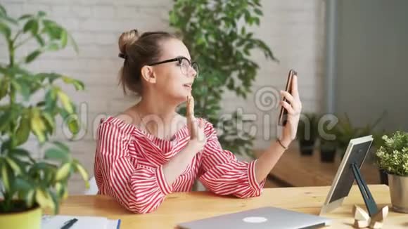 快乐女大学生通过手机打视频电话坐着笔记本电脑使用wifi的女性自由职业者视频的预览图