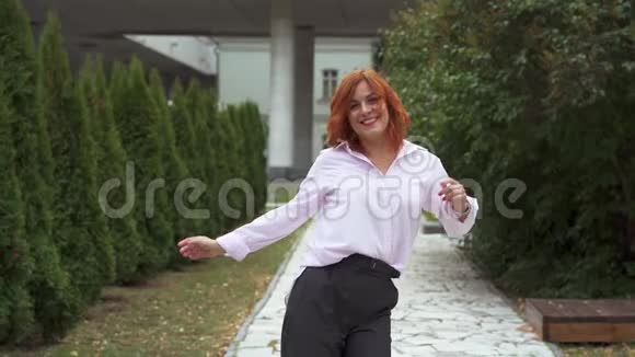 一个红头发的女人正在公园里跳舞她又笑又高兴心情很好视频的预览图