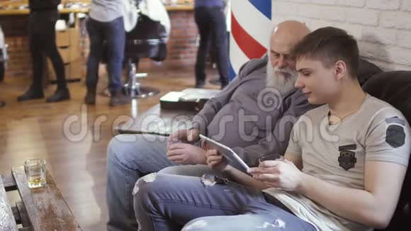 成熟的男人和年轻人在理发店使用数码平板电脑视频的预览图