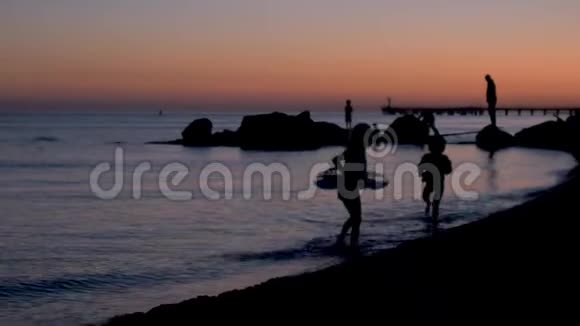 幼儿在日落时在海边的沙滩上玩石头孩子们在日落时在海滩上玩耍快乐视频的预览图
