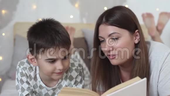 一个留着长发的漂亮女孩给躺在床上的小男孩读一本书然后吻他特写视频的预览图
