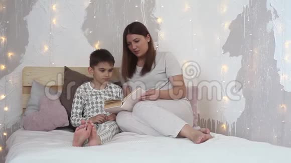 睡前穿着睡衣的漂亮女孩在床上给一个小男孩看书视频的预览图