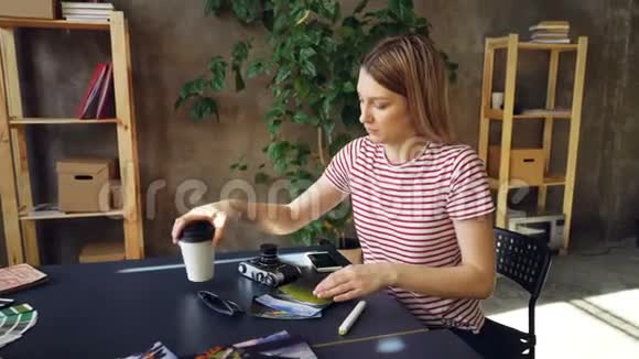 年轻女子正在整理照片外卖咖啡太阳镜专业相机和桌子上的标记并拍摄视频的预览图