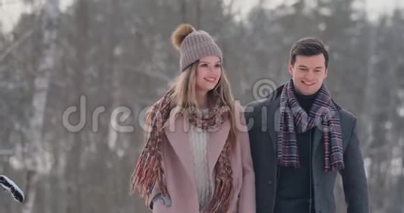 在冬天的雪林里穿着外套和围巾的年轻男女正在散步和玩可爱的一对视频的预览图