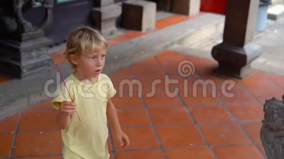 一个小男孩在佛寺里慢镜头在香炉里放一根芳香棒视频的预览图