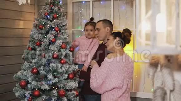 年轻幸福的家庭一起在门廊里缓慢地装饰圣诞树视频的预览图