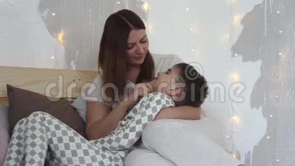 一位美丽的母亲和坐在床上的儿子玩吻他有一个好心情视频的预览图