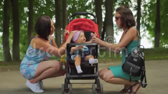 妈妈和她的朋友蹲在婴儿车里逗孩子开心视频的预览图