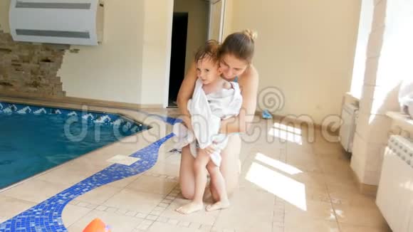 4k视频年轻微笑的母亲在游泳池游泳后用白毛巾将孩子裹在身上视频的预览图