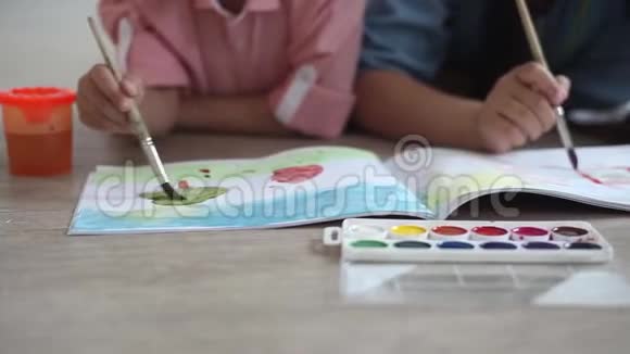 一个小男孩和一个小女孩在躺在地板上的相册上画着油漆特写视频的预览图
