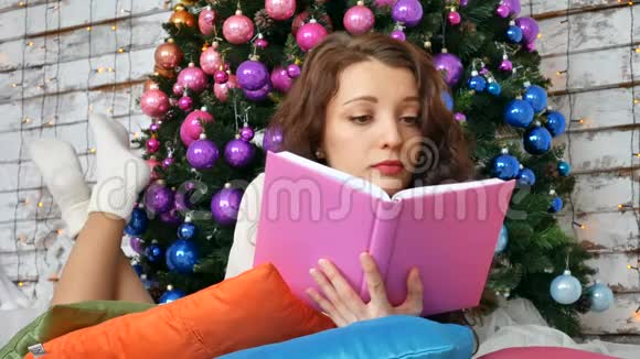 年轻的黑发正在阅读一本关于优雅圣诞树背景的书非常规色创意视频的预览图