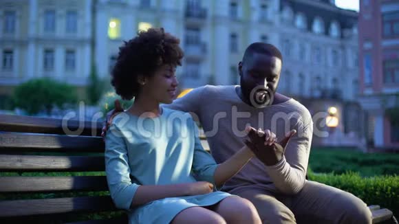 爱的男人抚摸女朋友的手在长凳上浪漫的约会在黄昏的城市视频的预览图