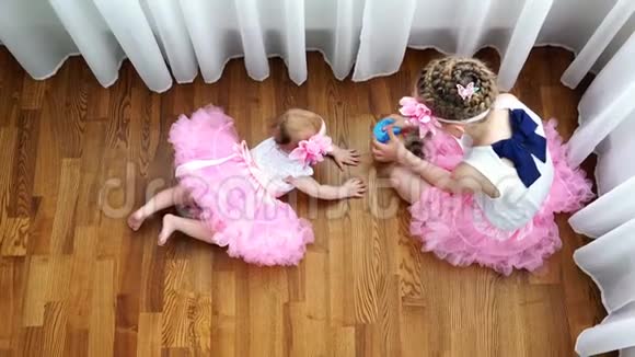 两个穿粉色裙子的姐妹在地板上玩玩具视频的预览图