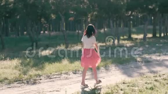 一个年轻漂亮的女人在森林里的路上在树叶间欢快地走着在阳光下闪闪发光视频的预览图