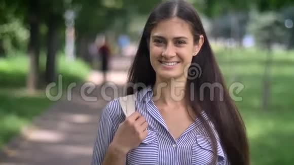 可爱快乐的年轻女学生站在公园里微笑着拿着背包视频的预览图
