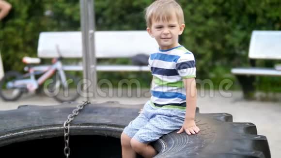 4k视频可爱的微笑幼儿男孩坐在大轮胎在公园操场视频的预览图
