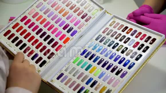 女人选择一种颜色在美容院画指甲各种颜色的指甲油测试仪的集合视频的预览图