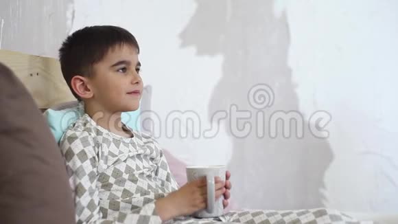 小男孩坐在床上喝着杯子里的茶视频的预览图