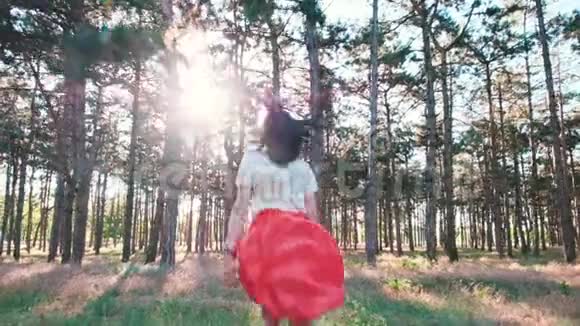 一个年轻漂亮的女人正高兴地在树林里的许多松树之间奔跑从后面看慢动作视频的预览图