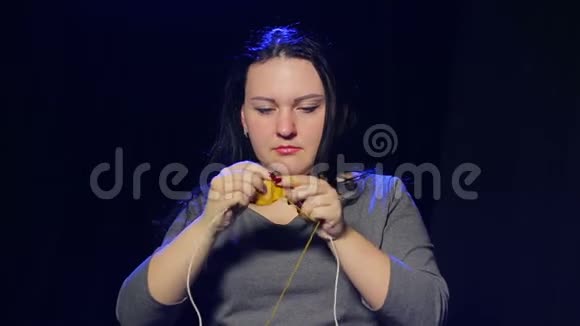 一个年轻的黑发女人穿着黑色背景的针织针用黄色线编织成圆形视频的预览图
