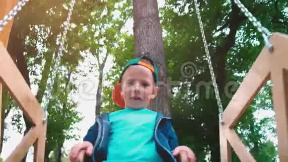 快乐的微笑男孩在一个木制的秋千上以一个宝座的形式在公园的阳光下一个孩子在秋千上玩得很开心视频的预览图