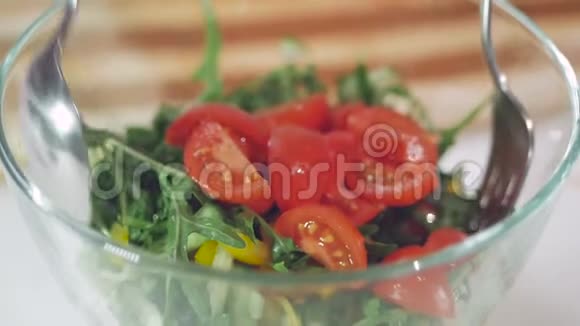 一个女人用玻璃碗折叠蔬菜沙拉原料的手的特写视频的预览图